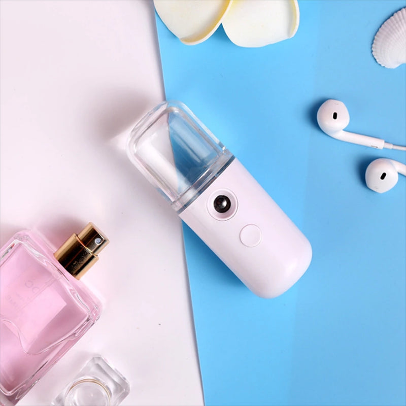 A travel-friendly handheld Piw Wee 30ml Mini Face Spray, placed on a blue and white surface alongside a perfume bottle and white earphones, ensures deep moisture for your skin. This compact sprayer by Piw Wee is perfect for on-the-go hydration.